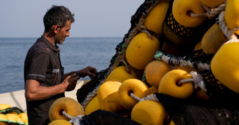 A worker on an industrial fishing boat repairs a net